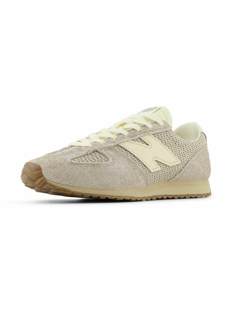 Beige suede shoes with mesh sides, yellow accents, and a rubber sole. Features a rounded toe and flat laces. Classic sneaker design.