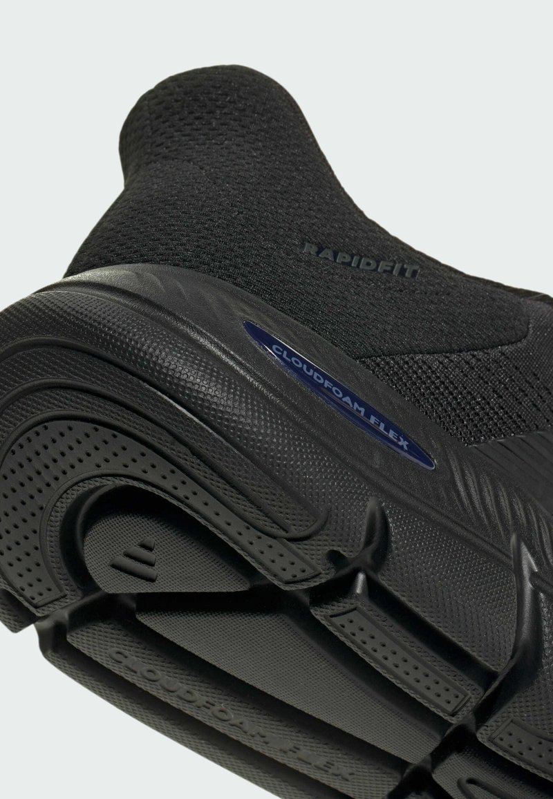 Chaussure de sport noire avec une tige tricotée sans coutures et une texture côtelée. La semelle comprend un label de technologie amortissante, "CLOUDFOAM FLEX".
