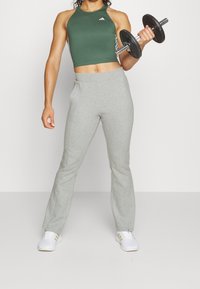 Grijze flared sweatpants met zakken, gecombineerd met een groene halter crop top met witte accenten. De persoon houdt een dumbbell vast.