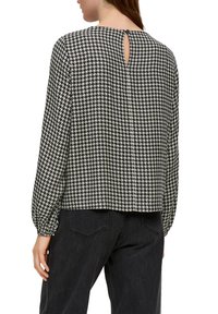 Langärmlige Bluse im schwarz-weißen Hahnentrittmuster, mit einem Schlüsselloch-Detail am Rücken und elastischen Bündchen. Weicher, strukturierter Stoff.