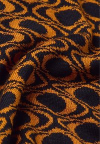 Strickstoff in Orange und Schwarz, mit einem kreisförmigen Muster. Die Textur ist glatt mit feinen Details, die das Design betonen.