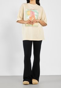 Camiseta oversize beige con un gráfico colorido de un tigre y un sol, combinada con pantalones acampanados negros de canalé y zapatos de slip-on marrones.