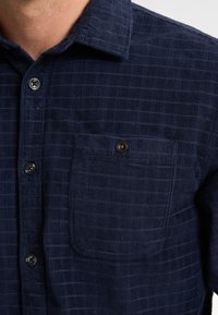 Navyblauwe corduroy shirt met een gestructureerde afwerking, voorzien van een button-down kraag, een voorzak en contrasterende knopen.