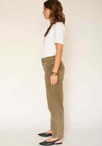 Pantalons en velours côtelé marron taille haute avec poches latérales, associés à un T-shirt blanc et des ballerines noires à bouts pointus ornées de motifs ronds.