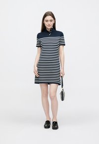 Marineblau-weiß gestreiftes Polokleid mit kurzen Ärmeln, Kragen, dreiknöpfiger Blende und leicht ausgestellter A-Linien-Form, kombiniert mit schwarzen Schuhen.