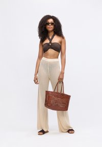 Brūns halter tops, bēšas acs plašas bikses, brūna austā rokassoma, melnas saules brilles un brūni plakanie sandales. Gluda tekstūra un brīvs piegriezums.