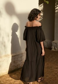 Juoda su pečių atvira suknelė, pagaminta iš lengvos medžiagos, su pūstomis rankovėmis, daugiasluoksniu apvadu ir laisvu siluetu. Minkšta tekstūra su elegantišku siluetu.
