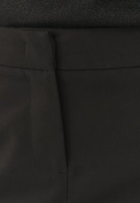 Černá látka zblízka, ukazující hladkou texturu a čisté linie; obsahuje pás se švem a minimálními designovými prvky.