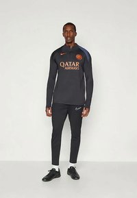 Tuta sportiva nera con logo arancione di Qatar Airways. Il top a maniche lunghe presenta un colletto alto e il baffo Nike, abbinato a pantaloni aderenti.