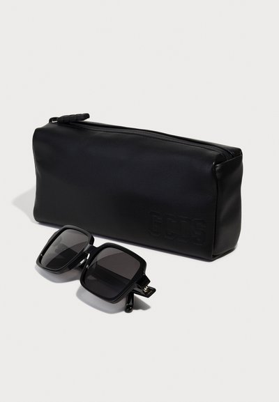 Étui à lunettes en cuir noir avec le logo "GCDS" en relief. Comprend des lunettes de soleil noires carrées avec des verres sombres et des montures larges et épaisses.