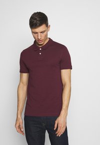 Bordeaux polo shirt van katoen, met een klassieke kraag, een knoopsluiting met drie knopen en korte mouwen. Geselecteerd met donkere spijkerbroeken.