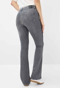 Jeans a zampa d'elefante in denim grigio con tasche posteriori, etichetta nera in vita e una texture di lavaggio chiaro. Abbinati a una maglietta casual e scarpe bianche.