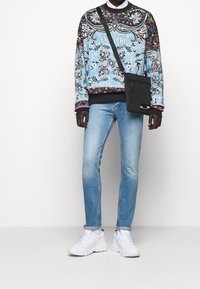 Blå mönstrad sweatshirt med blommönster, parat med ljusblå smala jeans och vita chunky sneakers. Svart crossbody-väska ingår.