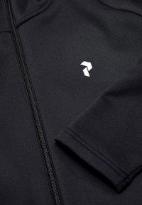 Crna zip-up hoodie od teksturiranog materijala, sa bijelim logom na području prsiju i glatkim zatvaračem. Uski, prilagođeni dizajn s manžetama.