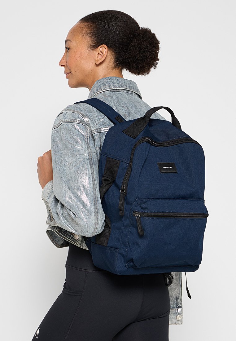 Mochila azul marino con dos compartimentos con cremallera, correas ajustables y tejido texturizado. Presenta acentos en negro y un parche con el logo.