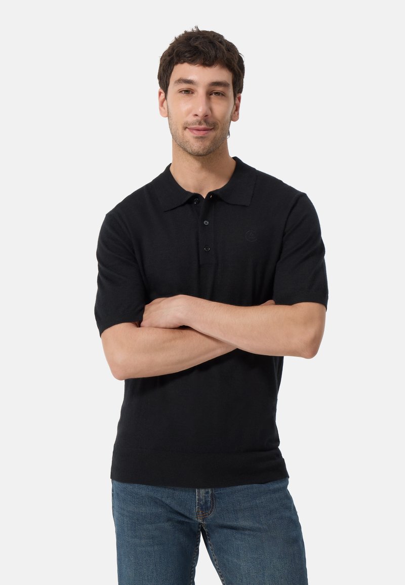 Svart kortärmad pikétröja, mjukt stickat tyg, med krage och treknäppning. Tajt passform, enkel utan mönster eller dekorationer.