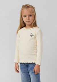 Kreemist ribidest pikkade varrukatega särk, millel on laineäär ja vasakul rinnal tikandiga hobuse kujutis. Kombineeritud siniste teksapükstega.