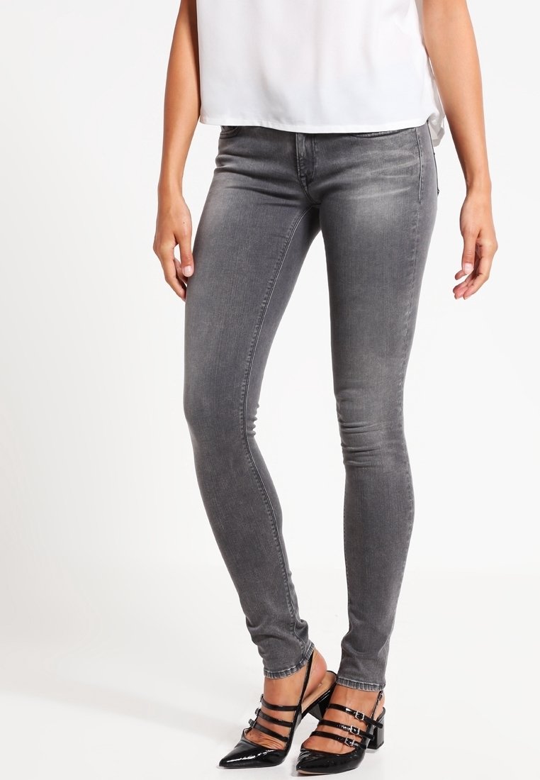 Jeans skinny grises con una textura de mezclilla suave, con una cintura de altura media y un leve desteñido, combinados con tacones de charol negros.