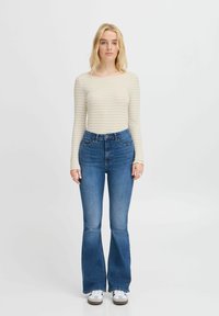 Randig beige långärmad topp som matchas med högmidjade, utsvängda blåjeans. Lätta vita sneakers med grå detaljer fulländar outfiten.