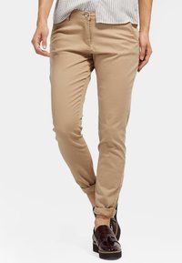 Béžové bavlněné kalhoty s úzkým střihem, s knoflíkovým zapínáním a předními kapsami, doplněné hnědými mokasínami.