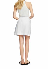 Falda blanca hasta la rodilla con un diseño simple, hecha de tela ligera, cuenta con un bolsillo trasero y está combinada con una blusa sin mangas y sandalias.