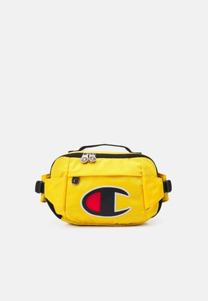 Banane jaune avec bordure noire, deux compartiments zippés, sangles réglables, et un grand logo noir, rouge et blanc sur la poche avant.