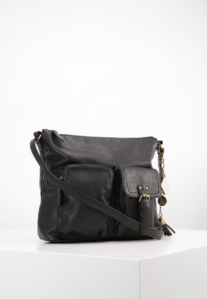 Černá kožená kabelka přes rameno s dvěma předními kapsami, z nichž jedna má klopu na přezku, a ozdobným přívěskem s třásněmi a kovovými doplňky.