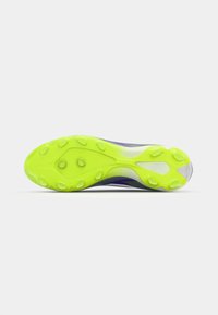 Textured sports shoe sole in bright neon yellow, featuring multidirectional studs for traction and a curved design for optimal performance.