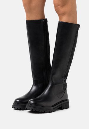 Botas negras hasta la rodilla con un frente de cuero liso, paneles de malla texturizada a los lados y suelas de goma resistentes para mayor tracción. Cierre con cremallera.