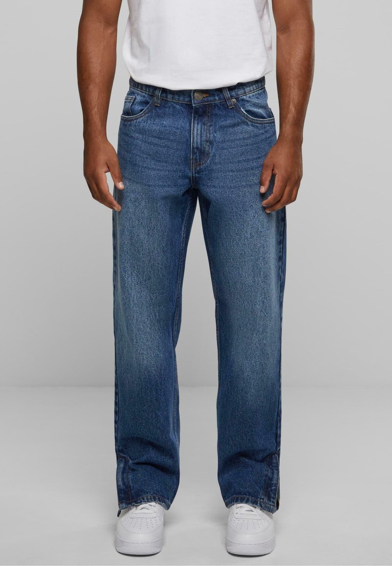 Donkerblauwe denim jeans met een relaxed fit, vijf zakken en een knoopsluiting. Heeft een vervaagde textuur en stiksel details langs de naden.