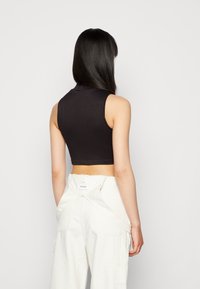 Top cropped preto, sem mangas, com um decote alto; textura canelada. Combinado com calças cargo brancas de cintura alta com detalhes de bolsos.