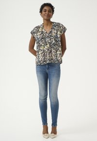 Blomstret bluse med korte ærmer i sort, creme og multicolor mønster, parret med lyseblå skinny jeans og creme farvede hæle.