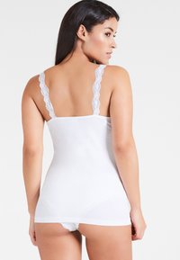 White tank top with spaghetti lace straps, fitted design, soft cotton material, and smooth texture; back view shows adjustable straps.