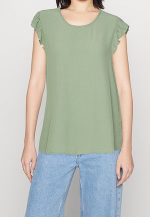 Top senza maniche verde oliva con dettagli arricciati sulle spalle, scollatura rotonda, tessuto morbido e vestibilità rilassata, abbinato a jeans azzurri chiari.