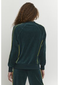 Felpa verde velluto con strisce laterali gialle, maniche raglan e polsini a costine. Tessuto morbido e vestibilità comoda, progettata per il massimo comfort.