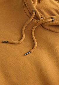Sudadera amarilla mostaza con capucha, que presenta cordones beige y ojales metálicos, mostrando un tejido suave y texturizado.
