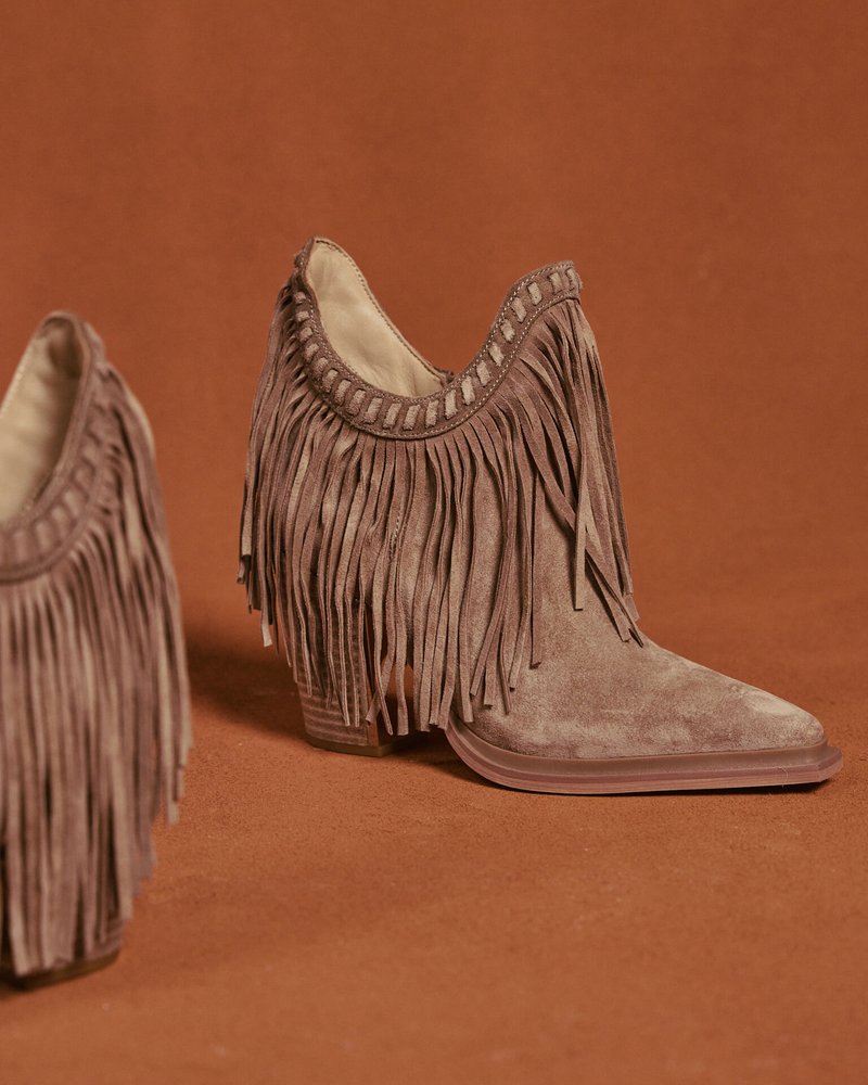 Botines con flecos en ante marrón claro, con punta afilada, tacón apilado y costuras decorativas a lo largo del borde superior.