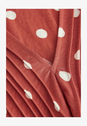 Hnědo-červená látka s bílými puntíky, s výstřihem do V a nařasenými sklady. Měkká textura s viditelným prošitím.