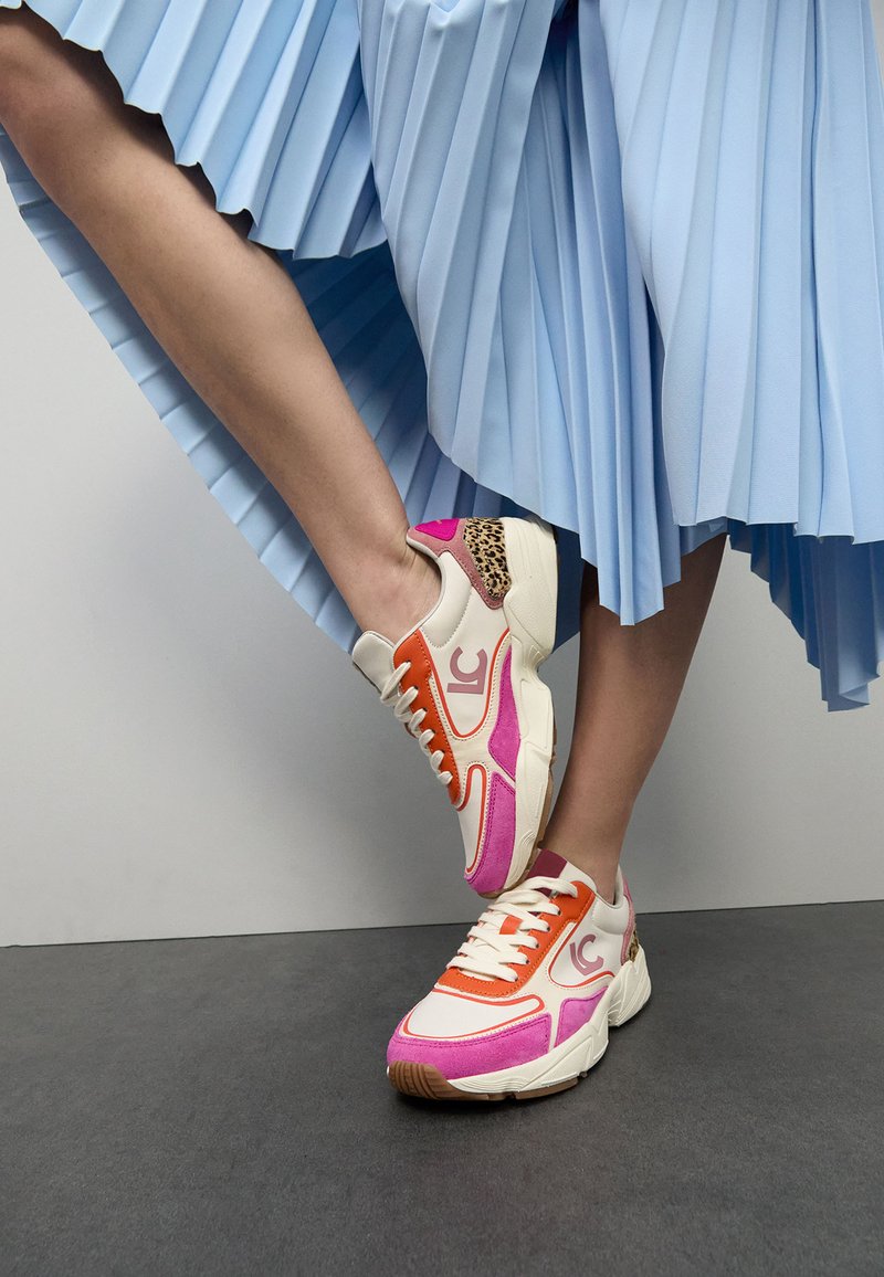 Zapatillas deportivas con una base blanca y acentos en naranja, rosa y leopardo. Suela gruesa, construcción texturizada y detalle del logo prominente.