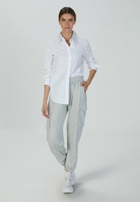 Weißes Hemd mit strukturiertem Kragen, kombiniert mit hellgrauen, glitzernden Cargo-Hosen mit Seitentaschen und elastischen Bündchen.