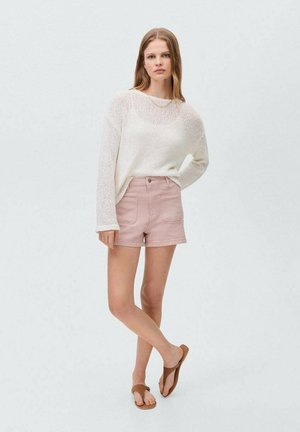Lehké bílé pletené svetřík s dlouhými rukávy, doplněný o růžové džíny šortky. Ploché hnědé sandály dokončují celý outfit.