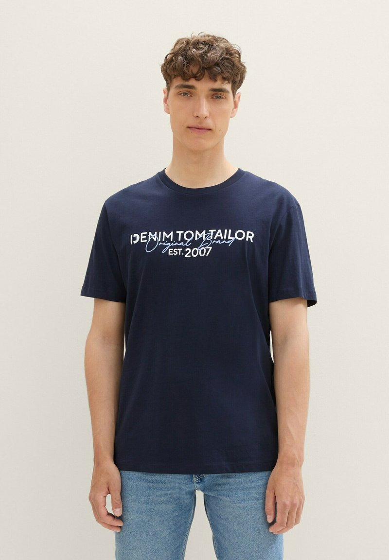 Camiseta de algodón azul marino con mangas cortas, que presenta el texto blanco "DENIM TOM TAILOR Marca Original EST. 2007" en la parte frontal.