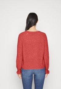 Rode gebreide trui met een ontspannen pasvorm, ronde hals en geribbelde manchetten. De textuur is zacht en heeft een iets losse weefsel. Gepaard met blauwe jeans.