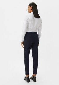 Witte overhemd met knopen, marineblauwe slim-fit broek en zwarte hakken. Gladde texturen, gedefinieerde naden en op maat gemaakte ontwerpelementen.