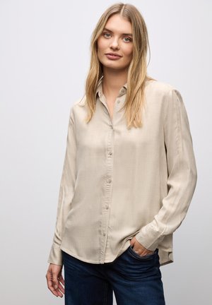 Beige långärmad skjorta med knappar, tillverkad av ett mjukt tyg, med klassisk krage och subtil textur, i kombination med mörka denimjeans.