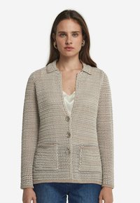 Beżowy szydełkowany kardigan z kołnierzykiem, przednimi kieszeniami i zapięciem na guziki. Teksturowany wzór dzianiny z luźnym krojem.