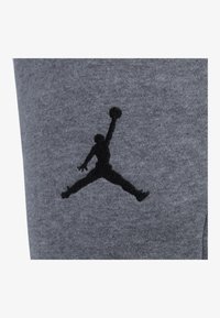 Szary materiał bluzy z kapturem z czarnym logo Jumpman, przedstawiającym sylwetkę gracza skaczącego z piłką koszykową.