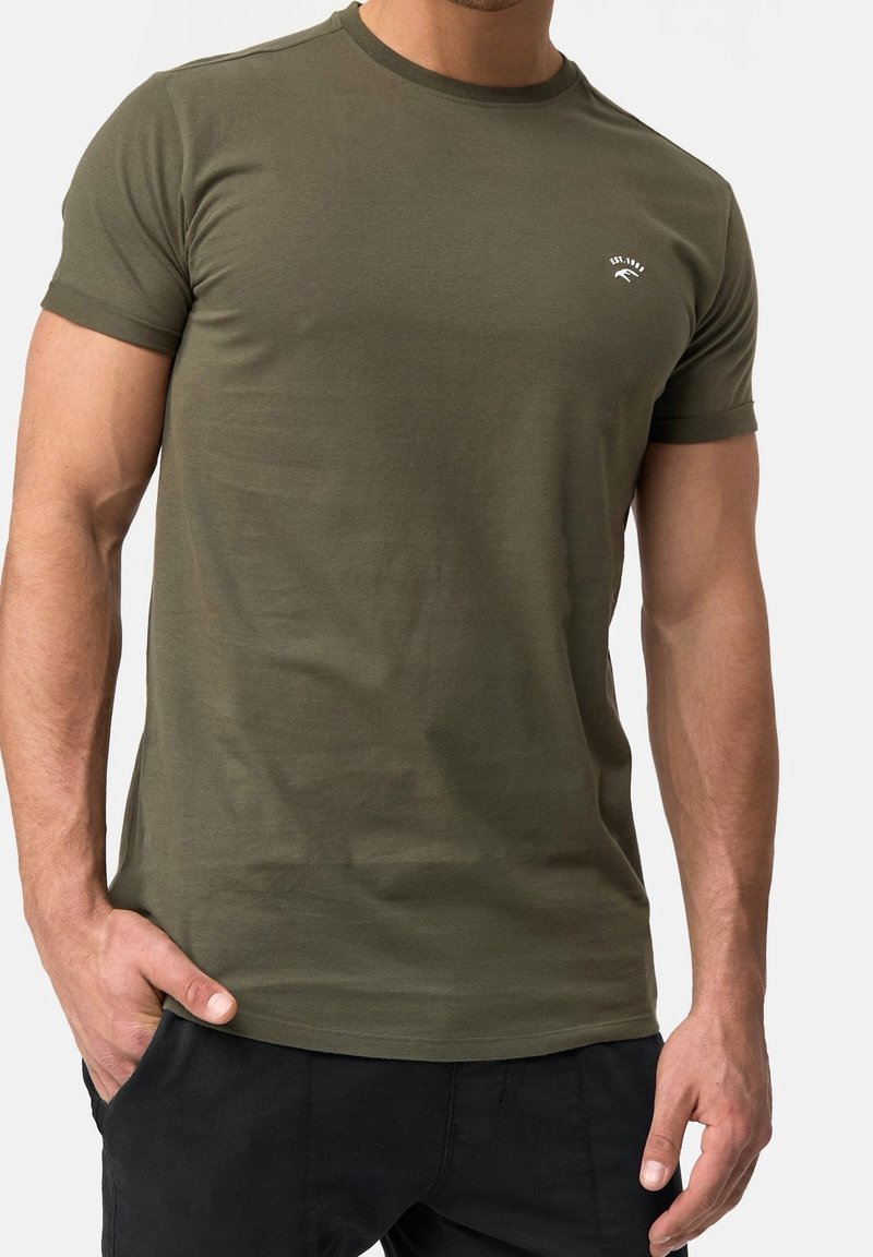 T-shirt en coton vert olive à manches courtes, col rond et petit logo blanc sur la poitrine. Texture lisse, design ajusté.