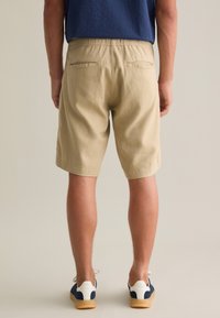 Shorts en coton beige avec un waistband élastique, deux poches arrière et une coupe décontractée, associés à des baskets sombres et un haut marine.