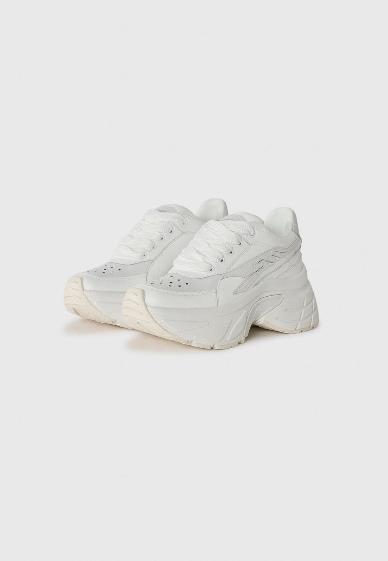 Ein Paar klobige weiße Sneakers mit dicken Sohlen, Schnürdesign, perforiertem Zehenbereich und dezenten seitlichen Details auf einem schlichten Hintergrund.